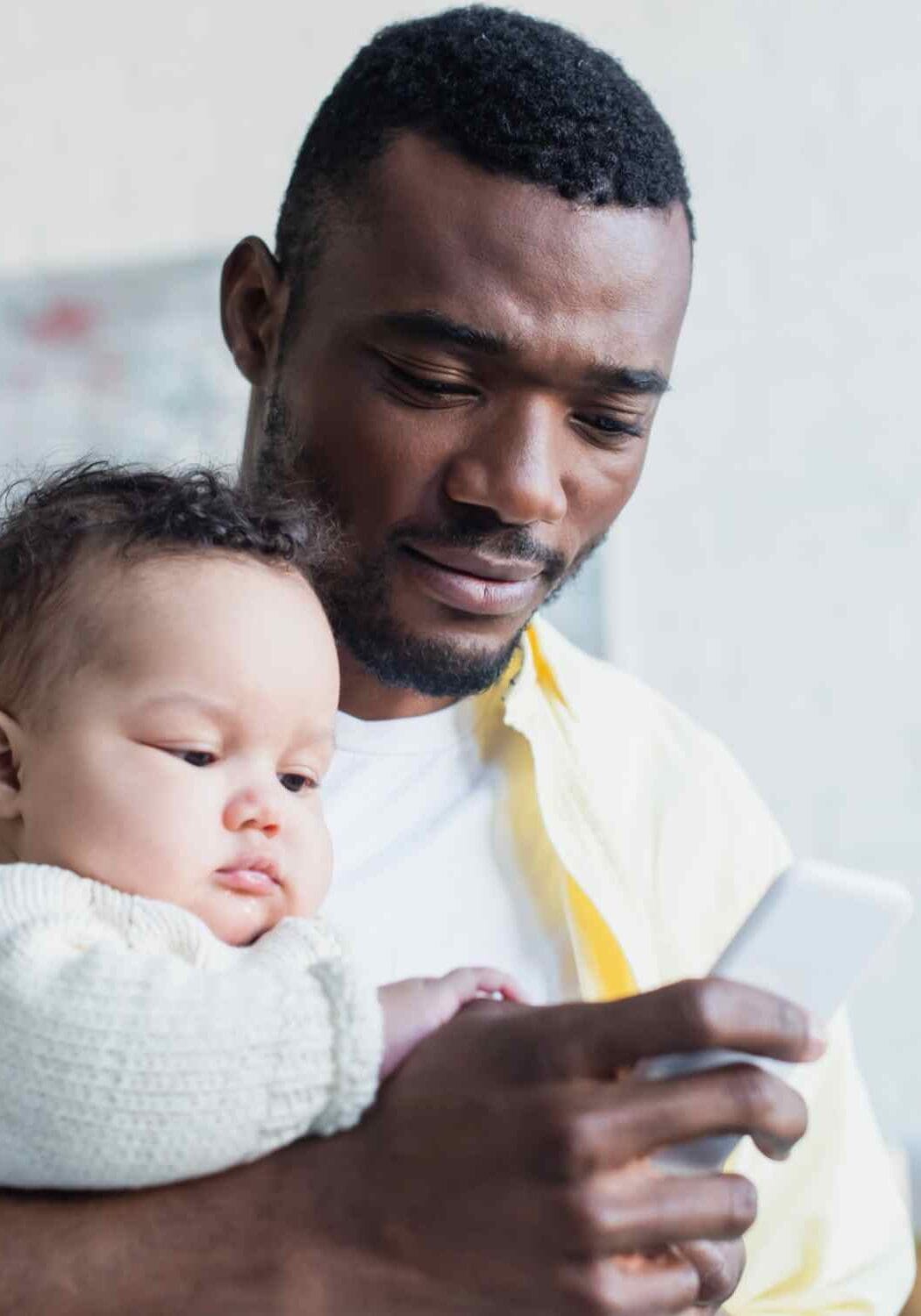 Pai mandando mensagem no celular com bebê nos braços