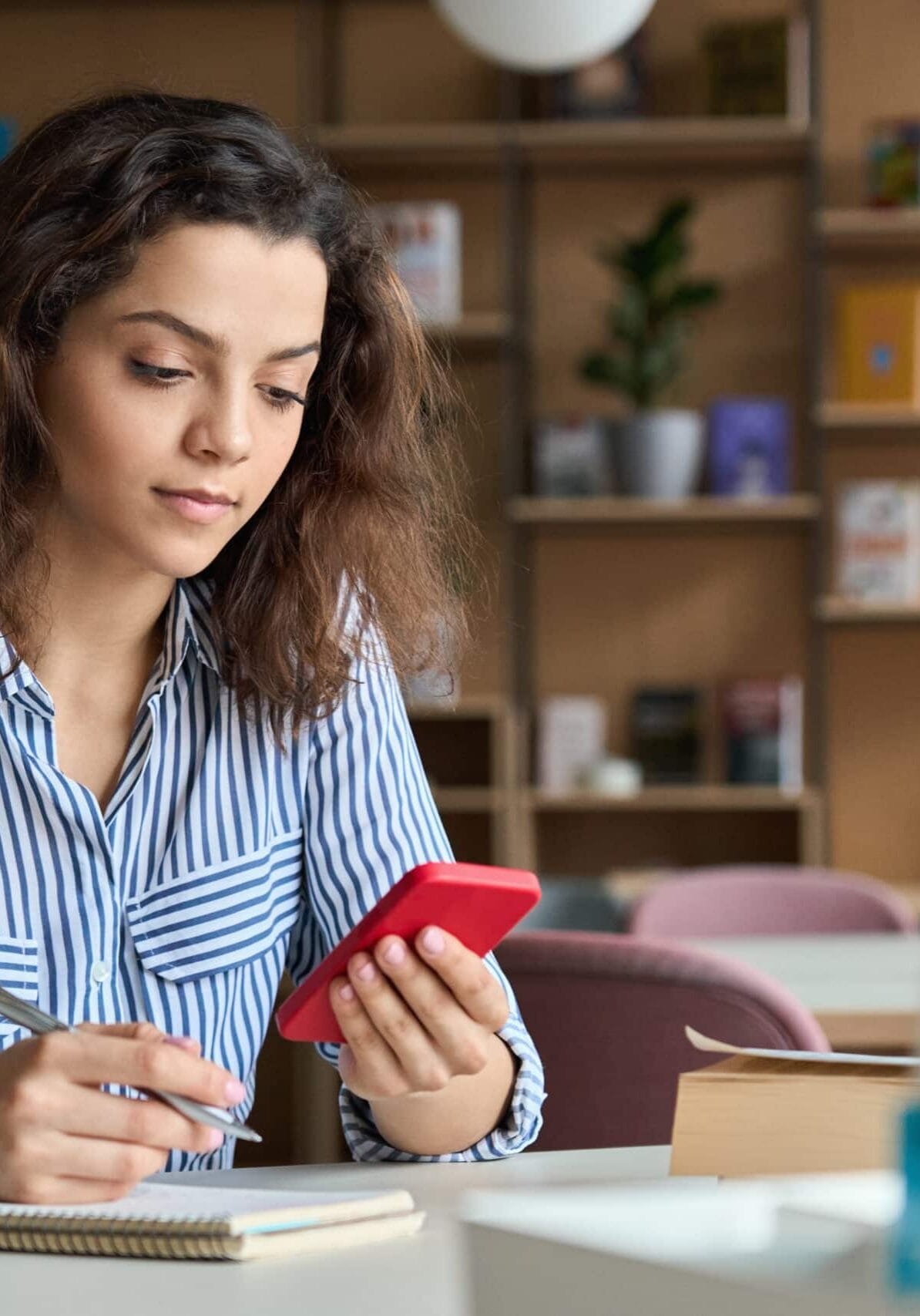 Menina olhando para o telefone com um bloco de notas e caneta