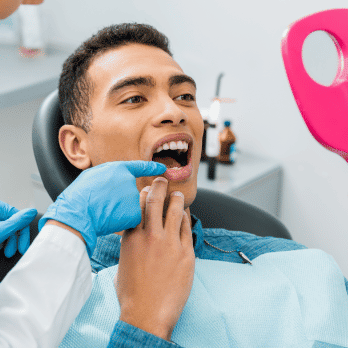 Homem no dentista segurando um espelho para olhar seus dentes